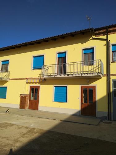 a yellow building with blue windows and a balcony at CASCINA PONTETTO in Asti