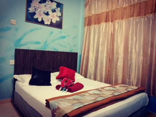 łóżko z czerwonymi poduszkami i wypchanym zwierzakiem w obiekcie Weng Kong Homestay w mieście Slim River