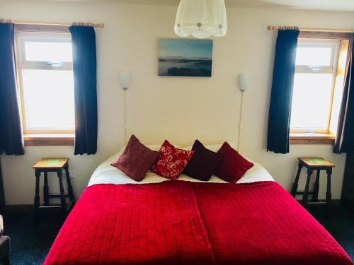 a bedroom with a red bed with two windows at Burnside Lodge in Portnahaven