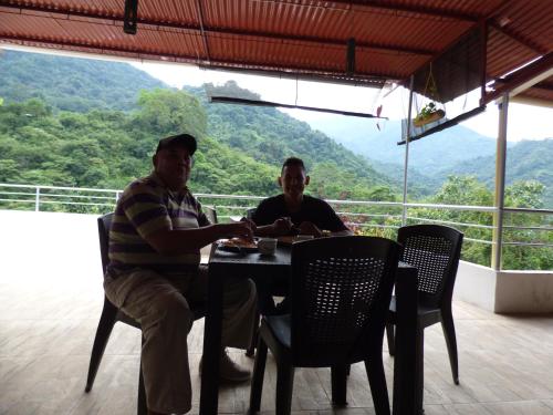 two men sitting at a table with a view of a mountain at Hostal Alto de la Montaña in Minca