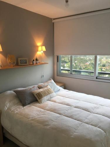 1 dormitorio con 1 cama blanca grande y ventana en Edificio Jardines del Country Piso 19 en Punta del Este