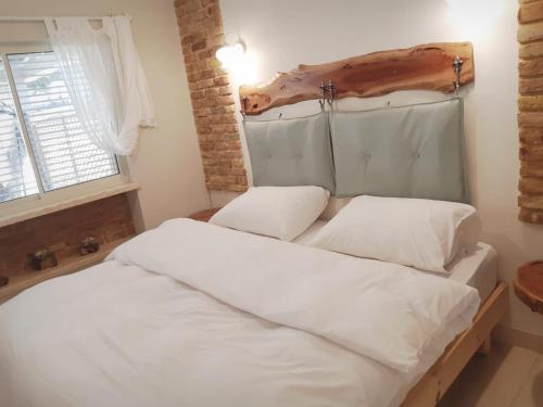 a bed with white sheets and a wooden headboard at חלון לגלבוע צימר בוטיק בעמק המעיינות in Bet Alfa