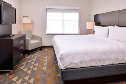 a hotel room with a large bed and a chair at Holiday Inn and Suites Addison by IHG in Addison