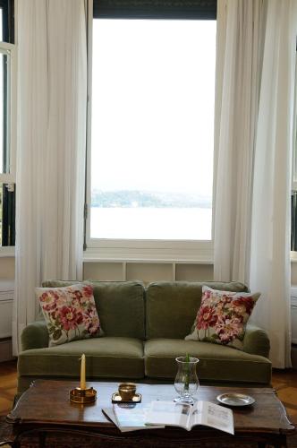a living room with a green couch in front of a large window at Villa Claudia dei Marchesi Dal Pozzo in Belgirate