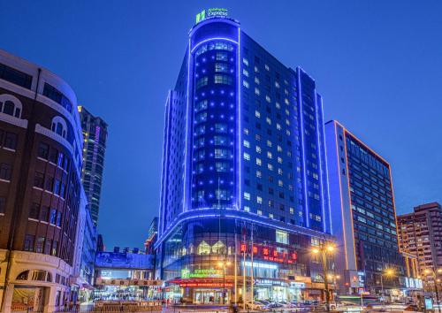 a tall blue building with lights in a city at Holiday Inn Express City Centre Dalian by IHG in Dalian