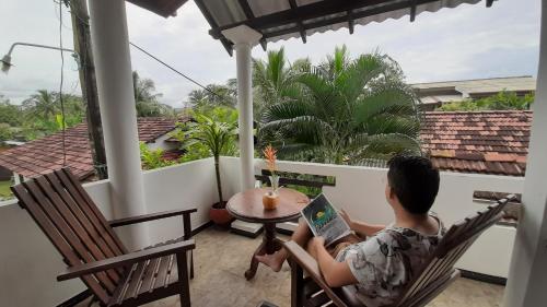 a boy sitting in a chair with a laptop on a balcony at Bandulas Beach House in Hikkaduwa