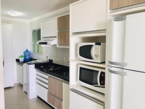 a kitchen with white cabinets and microwaves at Apartamentos Mediterrâneo Home Club in Bombinhas