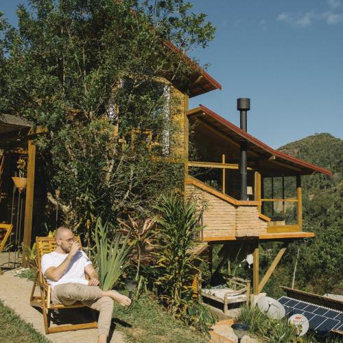 a man sitting in a chair in front of a house at Reserva Três Picos Chalés in Nova Friburgo
