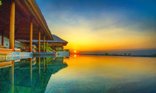 una puesta de sol sobre el agua al lado de un edificio en The Longhouse, Jimbaran - Bali, en Jimbaran