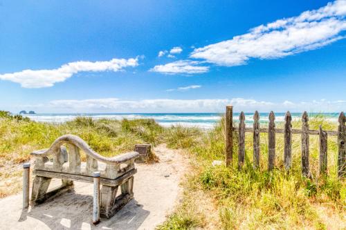 a wooden bench sitting on a beach next to a fence at Dolphin 1 in Rockaway Beach