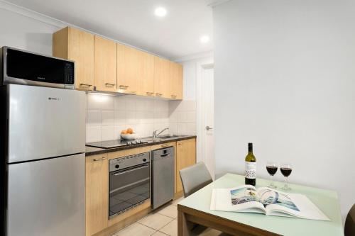 a kitchen with a white refrigerator and a table with wine glasses at Quest St Kilda Bayside in Melbourne