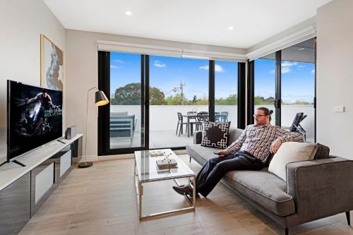 a man sitting on a couch in a living room at Manhattan Apartments - Glen Iris in Melbourne