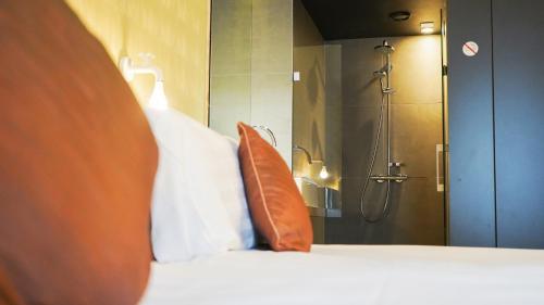 a bed with an orange pillow and a shower at Amosa Liège City Centre Hotel in Liège
