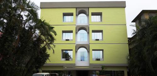 a yellow building with white windows and palm trees at Hotel Satkar in Katihār