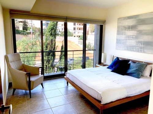 a bedroom with a bed and a chair and a large window at Sleek & Cozy Apartment with Pool & Patio In Abdoun in Amman