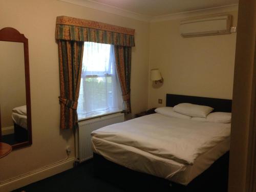 a bedroom with a bed and a mirror and a window at Abbey Lodge Hotel in High Wycombe