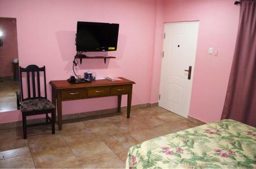 a bedroom with a desk and a tv on a pink wall at Piarco Village Suites in Piarco