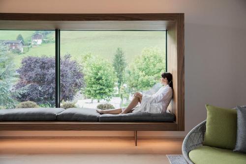 a woman sitting on a window sill looking out of it at Natürlich Hell. Aparthotel & Camping in Fügen