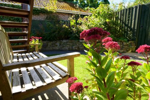 a wooden bench in a garden with pink flowers at Cottage Lodge Hotel in Brockenhurst