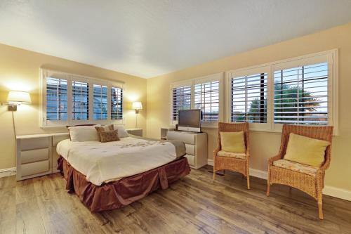 a bedroom with a bed and two chairs and windows at Boardwalk Dream in Santa Cruz