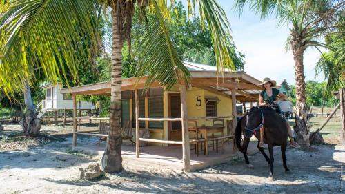 a woman riding a horse in front of a house at Horse Cottage in Sarteneja
