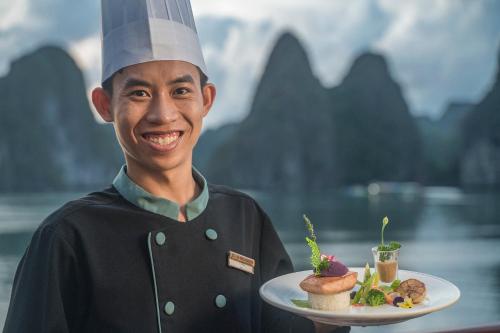 Heritage Line Ylang Cruise - Halong Bay & Lan Ha Bay في ها لونغ: رجل يرتدي زي طاهٍ يحمل طبق طعام