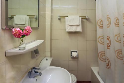 a bathroom with a sink and a toilet and a vase of flowers at Paradise Hotel Corfu in Gouvia
