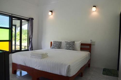 a bedroom with a bed with white sheets and a window at Nok Chan Mee Na in Chom Thong