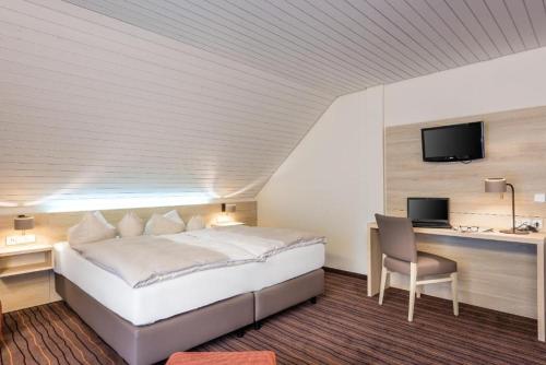 Schlafzimmer mit einem Bett, einem Schreibtisch und einem TV in der Unterkunft Business Class Hotel Häckermühle in Tiefenbronn