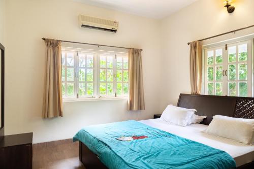 Schlafzimmer mit einem Bett mit blauer Bettwäsche und Fenstern in der Unterkunft Casa Arvana Near Calangute Beach in Calangute