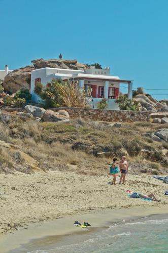 two people standing on a beach with a house in the background at Ydreos Studios & Apartments in Mikri Vigla