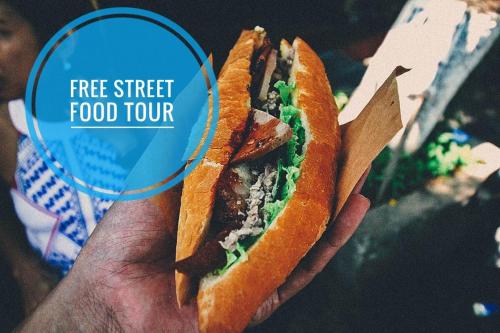 a hand holding a sandwich with a sign that says free street food tour at The Moon River Homestay & Villa in Hoi An