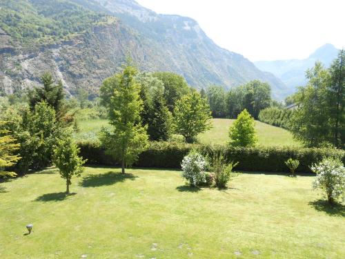 a field of grass with trees and mountains in the background at Le Chalet Carpe Diem in Le Bourg-dʼOisans
