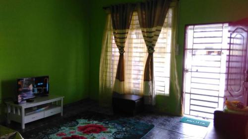 a living room with green walls and two windows at NUE Guesthouse in Kota Bharu