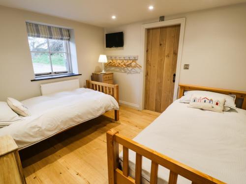 2 Betten in einem Zimmer mit Holzböden und einem Fenster in der Unterkunft Horseshoe Cottage in Pwllheli