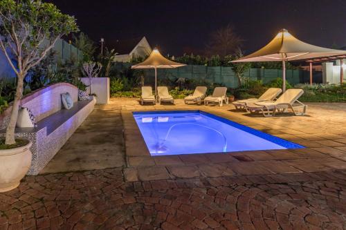 a swimming pool at night with chairs and umbrellas at Waterstone Lodge in Somerset West