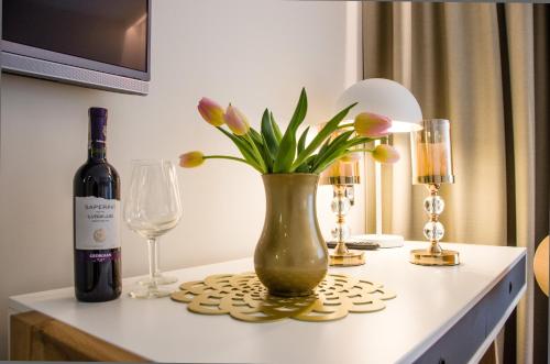 a vase with flowers and a bottle of wine on a table at Verde Apartments CENTRUM klimatyzacja in Koszalin