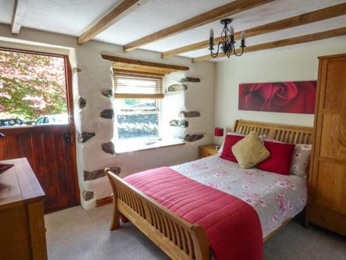 ein Schlafzimmer mit einem Bett mit roten Laken und einem Fenster in der Unterkunft Copper Beech Cottage in Coniston