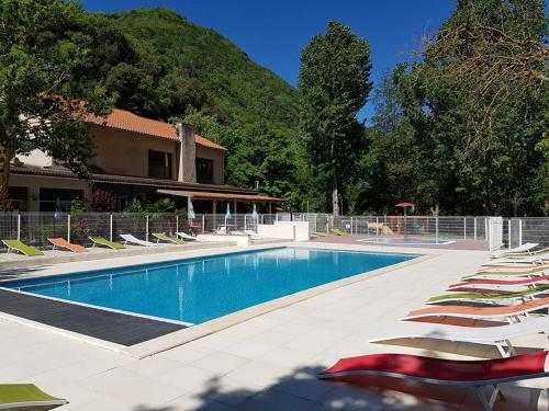 une piscine avec des chaises longues et un bâtiment dans l'établissement Le Moulin du Pont D'Aliès, à Axat