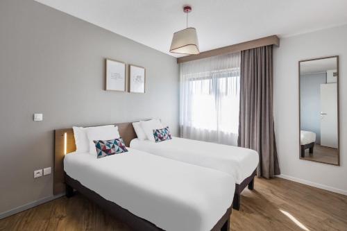 um quarto de hotel com duas camas e um espelho em Appart'City Confort Mulhouse em Mulhouse