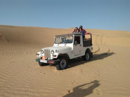 a white jeep driving through the desert with two people at Govind Hotel in Jodhpur