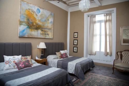 1 dormitorio con 2 camas, ventana y pintura en La Casa del Atrio en Querétaro