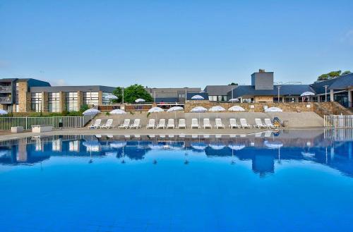 une grande piscine d'eau bleue avec des chaises et des bâtiments dans l'établissement Village Club Kerlannic, à Arzon