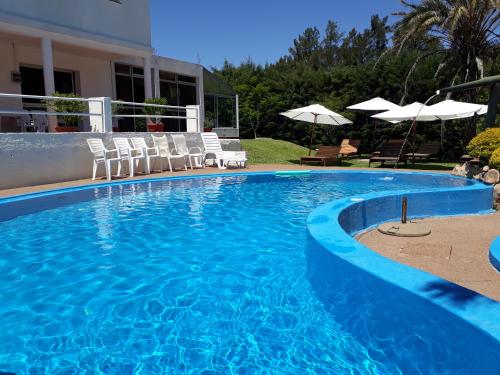a blue swimming pool with chairs and umbrellas at Hotel La Posta del Dayman in Termas del Daymán