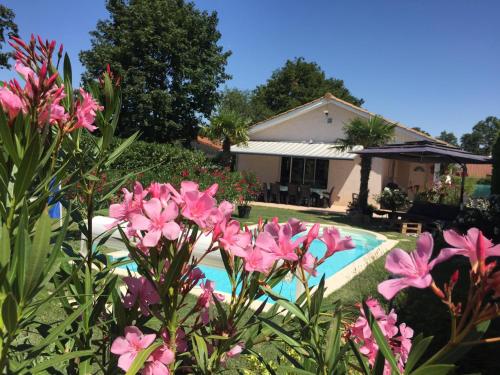 a swimming pool with pink flowers in front of a house at Les Tignoliers in Tignieu-Jameyzieu