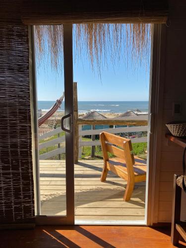 a door open to a deck with a bench on the beach at Cabañas Punta Papaya in Punta Del Diablo