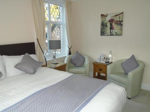 a bedroom with a bed and two chairs and a window at Trumbles Gatwick B&B in Charlwood