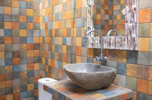 a bathroom with a bowl sink and a tiled wall at Uluwatu Kayana Bungalows by Bukit Vista in Uluwatu
