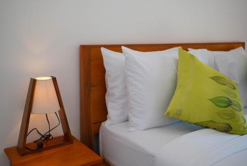 a bed with white pillows and a table with a lamp at Uluwatu Kayana Bungalows by Bukit Vista in Uluwatu