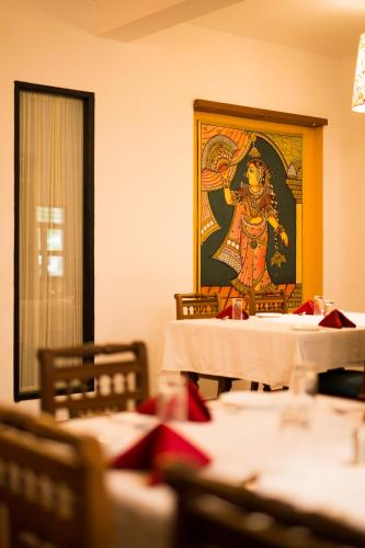 a dining room with tables and a painting on the wall at Mantra Koodam Kumbakonam - A CGH Earth Experience in Kumbakonam
